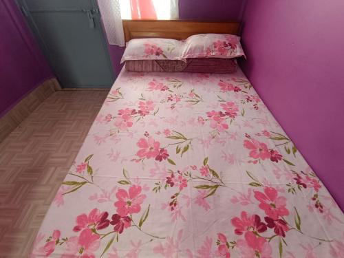a bed with a pink floral bedspread on it at Hala Rympei Homestay in Nongjrong