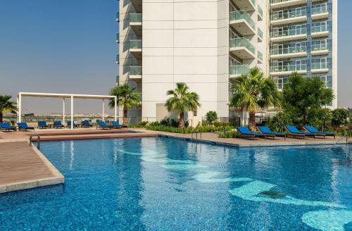 a swimming pool with blue chairs and a building at Radisson Dubai Damac Hills in Dubai
