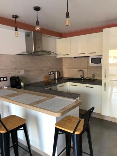 une cuisine avec des placards blancs et un îlot avec deux chaises dans l'établissement La Chrysalide, à Boëge