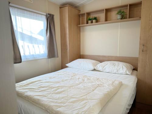 a bed with two pillows and a window in a room at Chalet 588 op Recreatiepark De Wielen in Sint Maarten