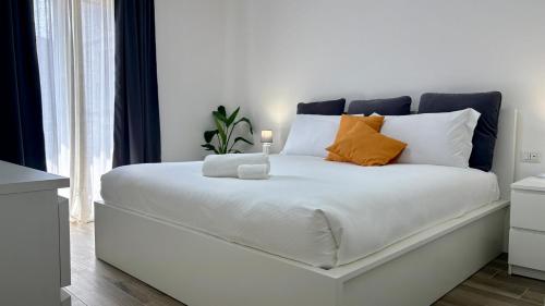 ein weißes Bett mit orangefarbenen Kissen und einer Kerze darauf in der Unterkunft Sciara Marina, Fiumefreddo di Sicilia, NUOVA STRUTTURA in Fiumefreddo di Sicilia