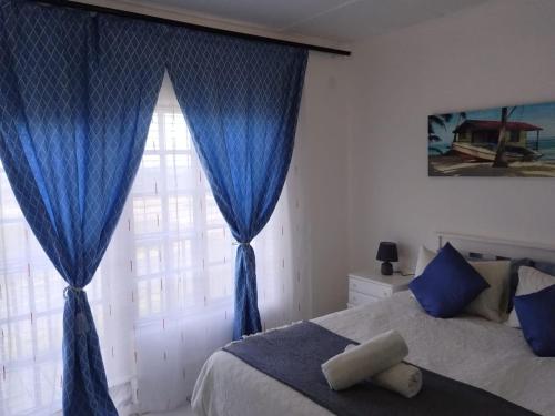 a bedroom with a bed with blue curtains and a window at Cosy Beach Vibes in Port Alfred