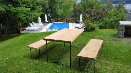 a table and two benches in a yard with a pool at Colina Del Manzano in Villa La Angostura