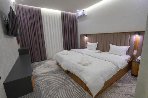 een slaapkamer met een groot bed met witte lakens bij Florence Hotel in Jizzax