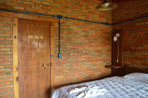 a brick walled bedroom with a bed and a wooden door at Pousada Alto Pirapitinga in Resende