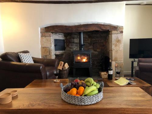 a table with a bowl of fruit in front of a fireplace at Church View Cottage & Barn in Hatherleigh