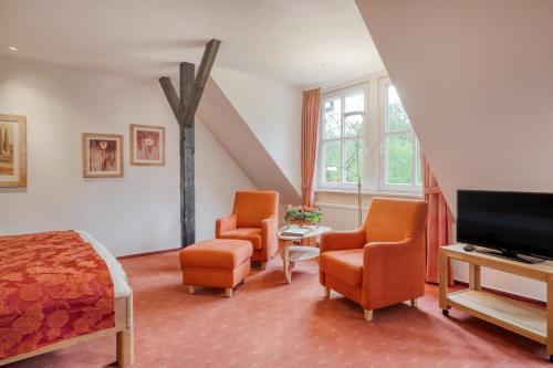 a bedroom with a bed and two chairs and a television at Landhotel Waldseiter Hof in Bad Bentheim