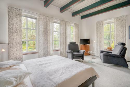 a bedroom with a bed and two chairs and windows at Landhotel Waldseiter Hof in Bad Bentheim