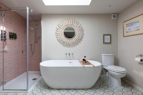 a bathroom with a tub and a toilet and a mirror at Nest Stay By The Butler Collection in Pulborough