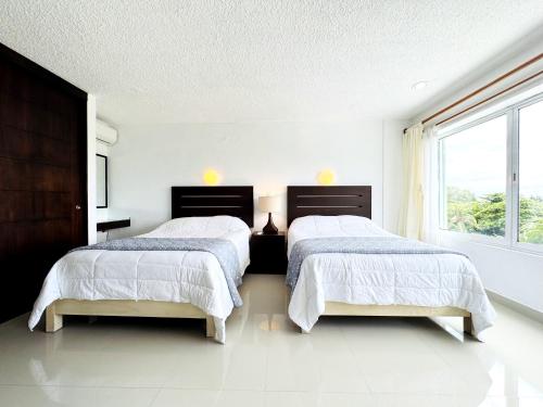 two beds in a white room with a window at Amplio Condo con acceso a playa - 6 Px in Cancún