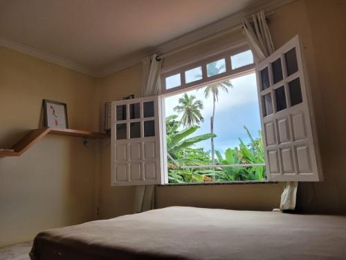 a bedroom with a window with a view of a palm tree at Cacha Pregos Vera Cruz - BA in Vera Cruz de Itaparica