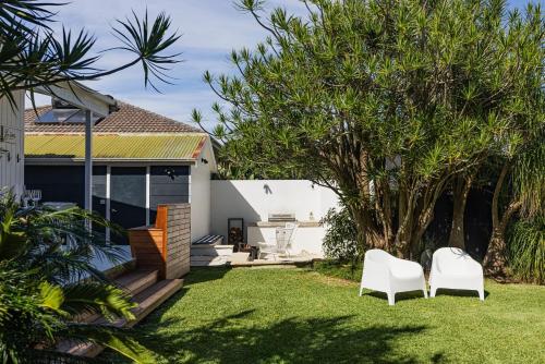 two white chairs in a yard next to a house at Ro-ana for 8, Gerringong in Gerringong
