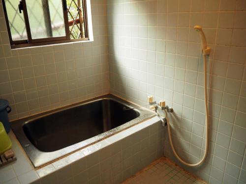 a bath tub in a tiled bathroom with a hose at 奄美大島 龍郷町 体験の宿 こうりゅう館 in Tatsugo