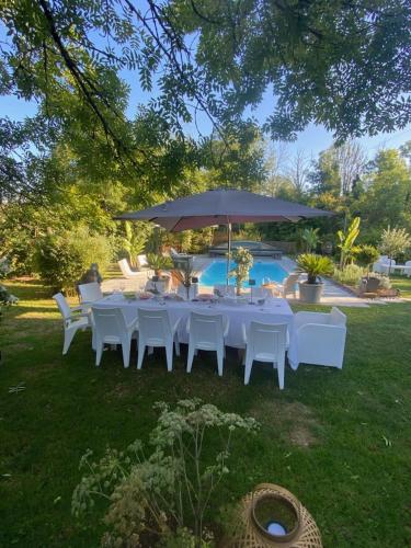 - une table avec des chaises blanches et un parasol à côté de la piscine dans l'établissement la maison de Etienne, à Chaux