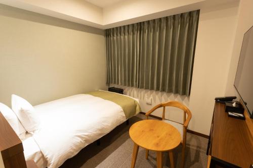 a bedroom with a bed and a table and a window at Hotel Sundays Amami in Amami