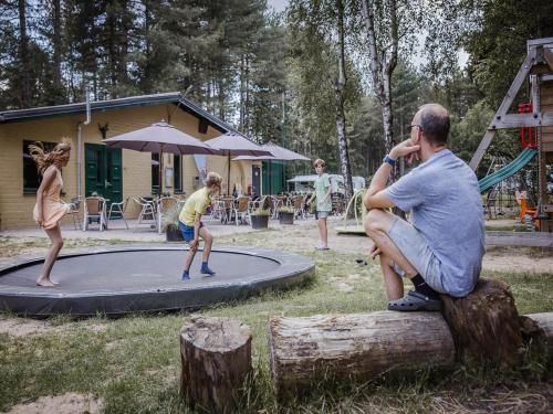 a man sitting on a log watching children playing on a trampoline at Chalet Escape in Antwerp in Beulk
