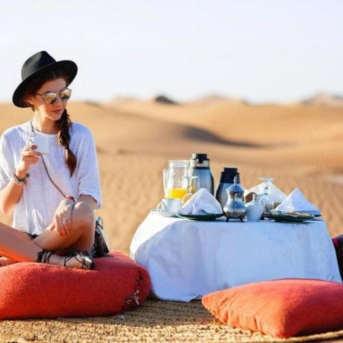 a woman sitting next to a table in the desert at Sahara Eyes Luxury Camp in Merzouga