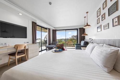 a bedroom with a large white bed with a desk and a tv at Golden Tulip Pattaya Beachfront Resort in Pattaya North