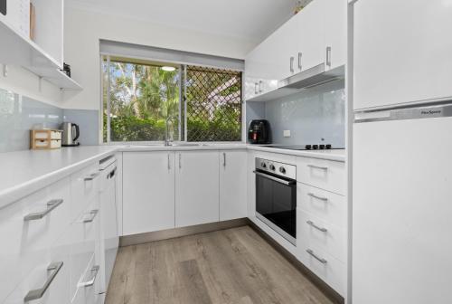 a white kitchen with white cabinets and a window at 2 Bedroom Villa In Tropical Resort in Noosaville