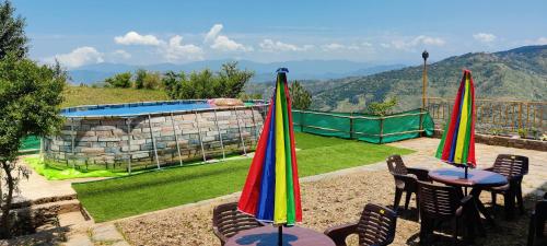 two tables and chairs with umbrellas next to a pool at Orchard Green Dummi in Nāldera