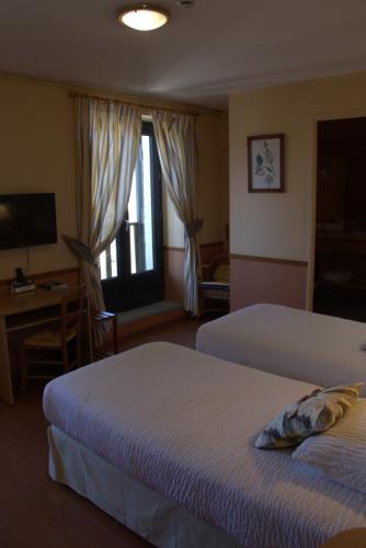 a hotel room with two beds and a desk and a window at Hotel Restaurant La Clairiere in Chambon-sur-Dolore