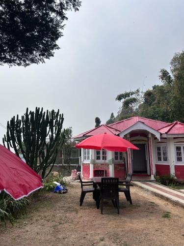 a table with a red umbrella in front of a house at Maliani Farms in Takdāh
