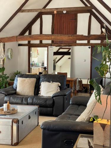 a living room with a black leather couch at Milk Barn - Rustic farm stay in Great Chart