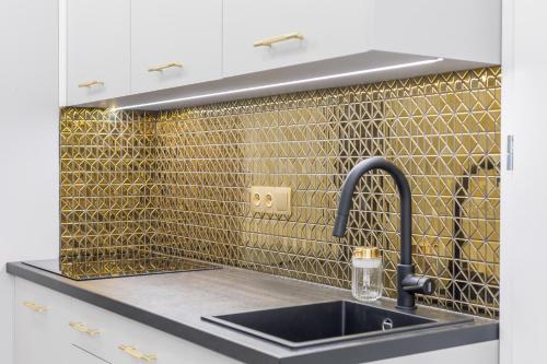 una cocina con fregadero y una pared de azulejos de oro en Exclusive Panoramic APARTMENT, en Cracovia