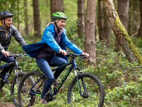 a man and woman riding bikes in the woods at Thorpe Forest Cabins - Forest Holidays in Thetford