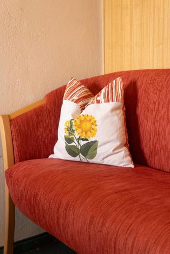 a red couch with a pillow with a flower on it at Pension Trillerhof in Ramsau am Dachstein
