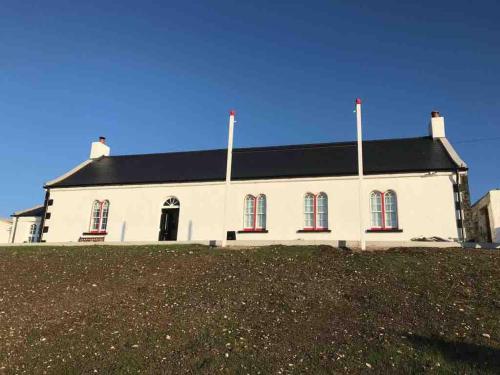 a large white building with red windows on a hill at Ballintoy old school house in Ballintoy
