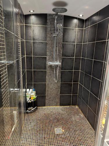 La salle de bains est pourvue d'une douche et de murs carrelés noirs. dans l'établissement Vue mer - Appartement 7 personnes, à Saintes-Maries-de-la-Mer