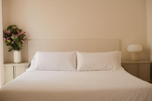 ein weißes Bett mit weißer Bettwäsche und einer Vase aus Blumen in der Unterkunft CASA SIRFANTAS Málaga in Málaga