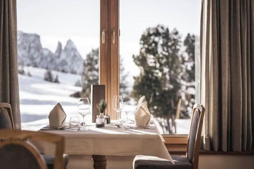 a table with wine glasses and a window with snow at Hotel Steger-Dellai in Alpe di Siusi