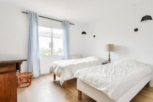 two beds in a white room with a window at Maison pour 6 avec jardin - 800 m de la plage in La Guérinière