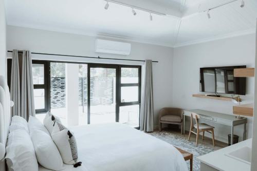 a white bedroom with a bed and a desk at Cornerstone Manor Kathu in Kathu