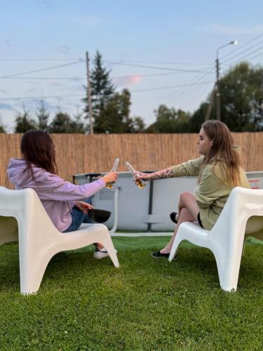 two women sitting on white chairs in the grass at Apartamenty Wisła Krzywa 8, wanna z hydromasażem, basen zewnętrzny in Wisła