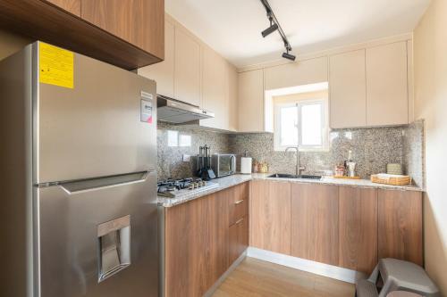 a kitchen with a stainless steel refrigerator and wooden cabinets at Elegante y versátil apartamento en Ensanche Ozama SDE in Calero