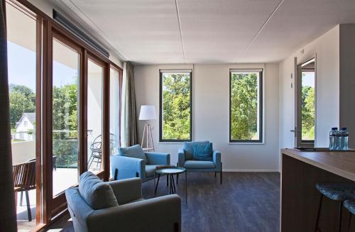 a living room with blue chairs and windows at Strandhotel Duinoord in Vrouwenpolder