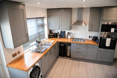 a kitchen with gray cabinets and a wooden counter top at Stylish 3Bed House with Garden, near Stations, London & Harry Potter studios, great for families and contractors in Watford West Station