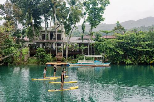three people on surfboards in the water in front of a house at Loboc Riverside Inn & Restaurant in Loboc