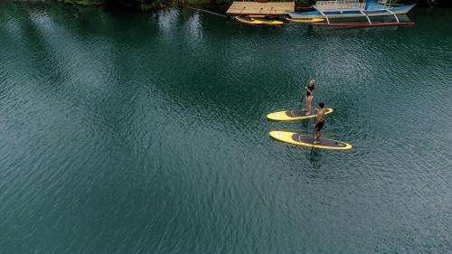 two people are standing on surfboards in the water at Loboc Riverside Inn & Restaurant in Loboc