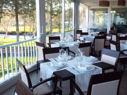 un restaurante con mesas y sillas blancas y ventanas en Hotel Ansuiña en Baños de Molgas