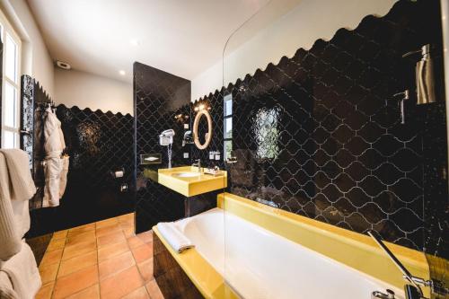a bathroom with a white tub and a black tile wall at Le Palais d'Aglaé, Hôtel de Charme in Gordes