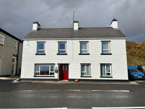 a white house with a red door on a street at Mary's of Mulranny in Mulranny