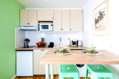 une cuisine avec des placards blancs et une table en bois avec des tabourets dans l'établissement La Paillote - Parking privé - Lit King Size, à Corbeil-Essonnes