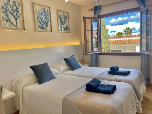 two beds in a room with a window at Oasis Calan Porter con piscinas y junto la playa in Cala'n Porter