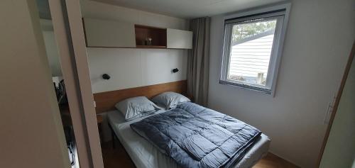 un petit lit dans une chambre avec une fenêtre dans l'établissement MH 148, camping bois dormant, 2ch, 4 pers, à Saint-Jean-de-Monts