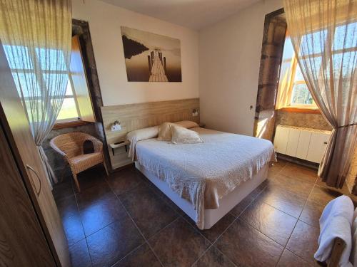 a bedroom with a bed and a chair and windows at Albergue Rectoral San Mamede da Pena EXCLUSIVE FOR PILGRIMS in Negreira