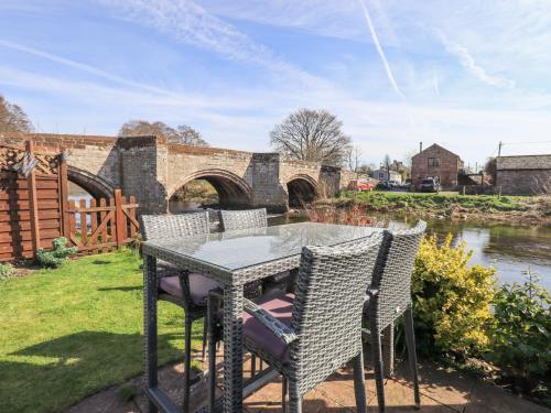 a table and chairs on a patio next to a river at Beckside Cottage in Penrith